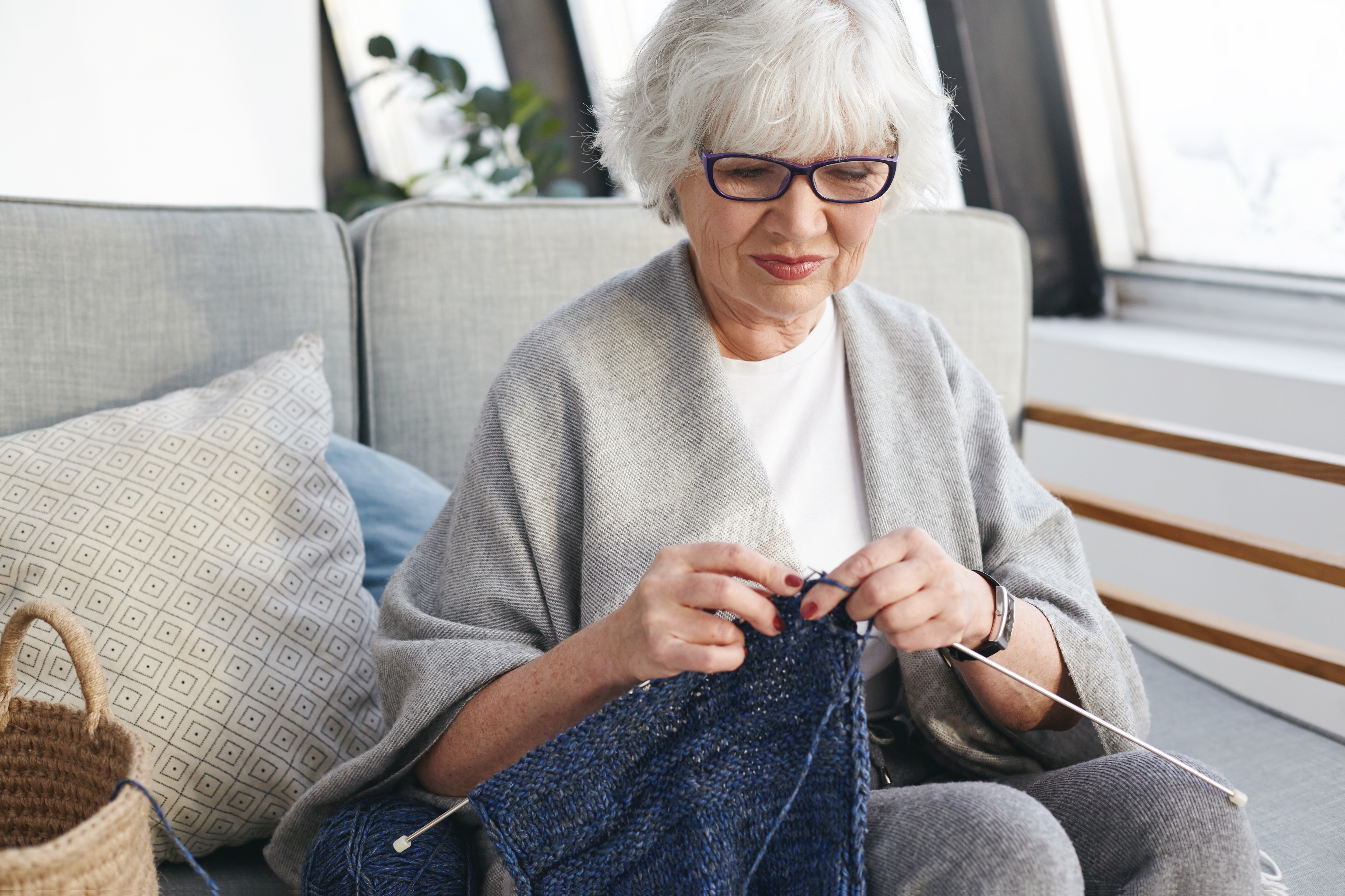active-talented-woman-retirement-spending-day-indoors-knitting-warm-clothes-grandchildren-sitting-sofa-cozy-interior-smiling-needlework